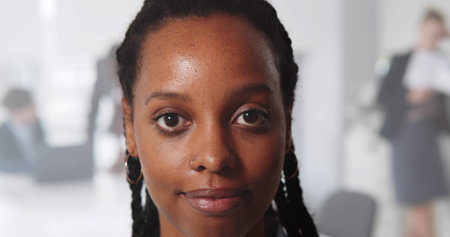 Close up portrait of smiling black young woman looking at camera standing inside modern office