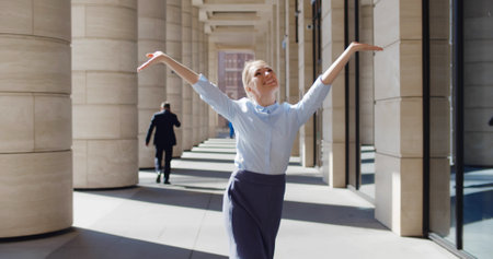 Happy successful young businesswoman dancing outside business center celebrating promotionの写真素材