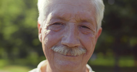 Bokeh close up portrait of happy senior man looking at camera outdoorsの写真素材