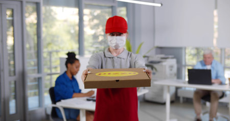 Delivery woman in face mask and gloves with pizza boxes at officeの写真素材