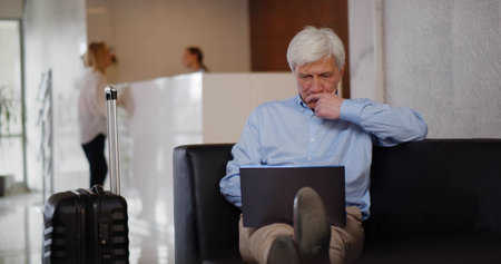 Concentrated mature businessman using laptop computer in hotel lobbyの写真素材
