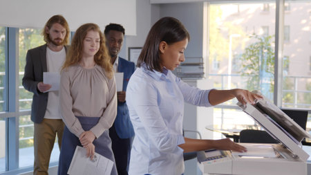 Group of young managers standing in queue for copier at officeの写真素材