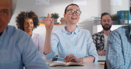 Young woman in glasses attending education courses and raising hand to ask questionsの写真素材