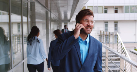 Handsome young businessman walking with mobile phone in front of office buildingの写真素材