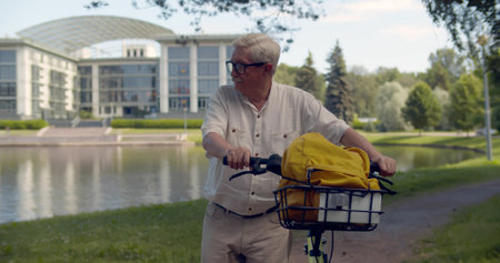 Elderly man walking at public park dragging bicycle by hand.の写真素材