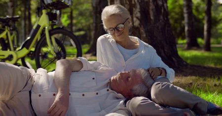 Portrait of happy retired couple relaxing on grass in summer park