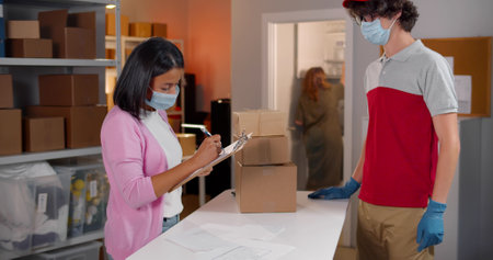 Deliveryman in face protective medical mask and gloves take parcel box in warehouseの写真素材