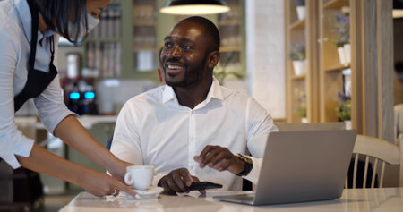Waitress in safety mask serve coffee for businessman in restaurantの写真素材