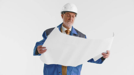 Happy elderly construction manager reading paper blueprint isolated on white backgroundの写真素材