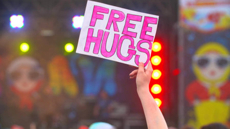 young girl holds free hugs poster at concert and dance