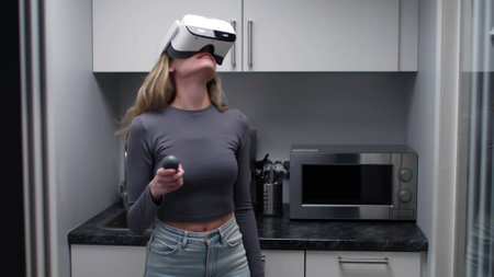 Young woman wearing vr headset and using joystick standing in small kitchen