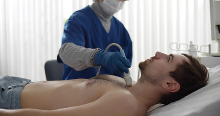 Doctor in safety mask and gloves performing thyroid ultrasound test on male patient