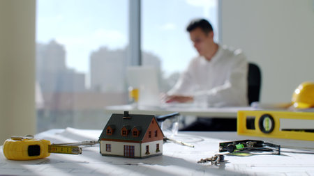 Architect tools and house model on table with man working on blurred background