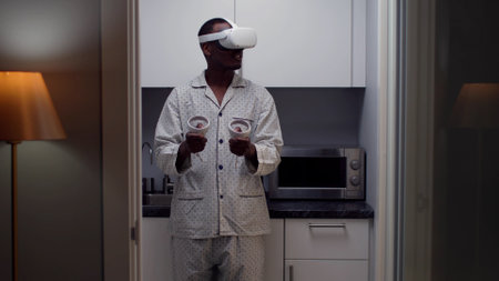 African-American man in pajamas play video game using vr goggles and controllersの写真素材