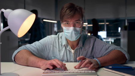 Male executive in safety mask work on computer in modern officeの写真素材