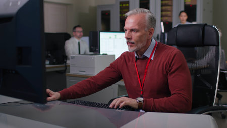 Mature engineer sit down at desk and type on computer in modern officeの写真素材