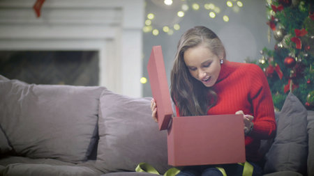 Beautiful woman sitting on couch and opening New Year present boxの写真素材
