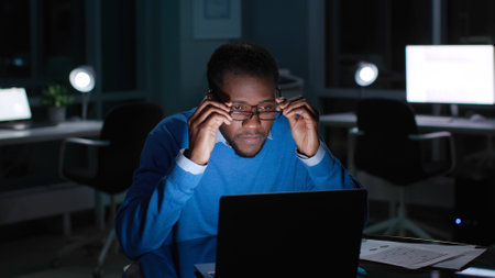 African-American manager in glasses read email on laptop working late in eveningの写真素材