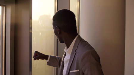 Young black businessman looking out of window in office