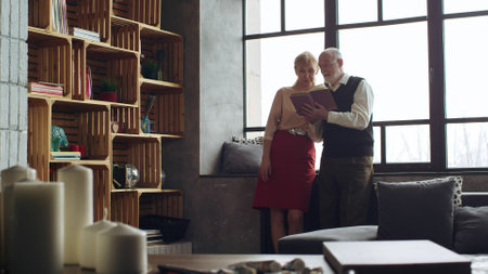 Senior couple reading book together in living roomの写真素材