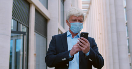 Senior manager using smartphone outdoor wearing safety maskの写真素材