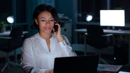 Portrait of successful African-American businesswoman talk on smartphone working late in officeの写真素材