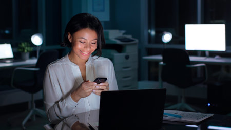 African-American businesswoman read sms on cellphone and smile working late in officeの写真素材