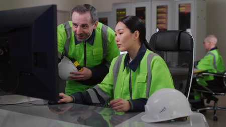 Mature foreman in uniform help young asian woman engineer working on computerの写真素材