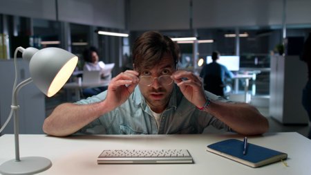 Portrait of shocked businessman staring at computer screen working late in officeの写真素材
