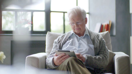 Senior man using digital tablet sitting on the couch at homeの写真素材