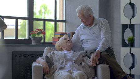Romantic senior couple smiling while sitting on sofa at homeの写真素材