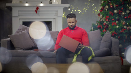 Disappointed man open Christmas present in living room.の写真素材