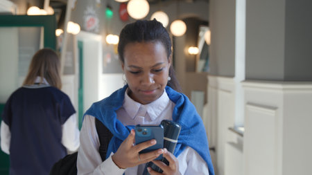 African-American teen girl with smartphone and backpack walk in schoolの写真素材