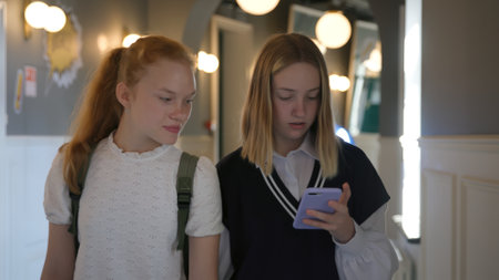 Schoolgirls use smartphone and talk walking in school corridorの写真素材