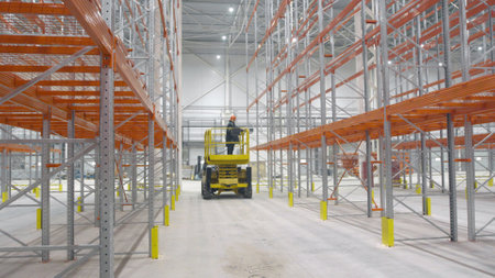 Distribution warehouse hall with engineer on hydraulic scissors lift platformの写真素材