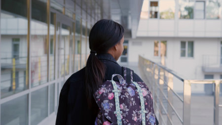 Back view of African-American schoolgirl with backpack walk outdoors. Girl student walking outside school buildingの写真素材
