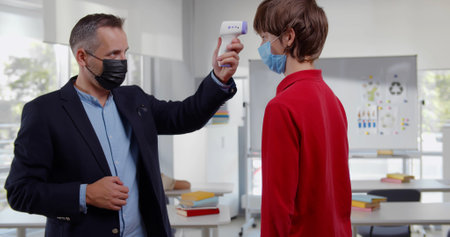 Portrait of male teacher checking temperature of children entering classroom in school