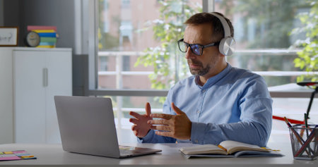 Mature teacher in headphones having online class on laptopの写真素材
