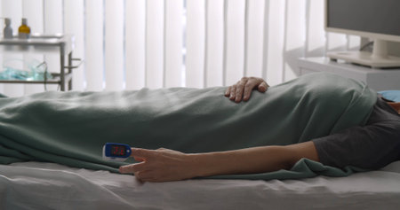 Patient with fingertip pulse oximeter lying in hospital bedの写真素材