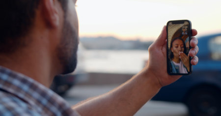View over shoulder of young man doing video call using smartphone at city