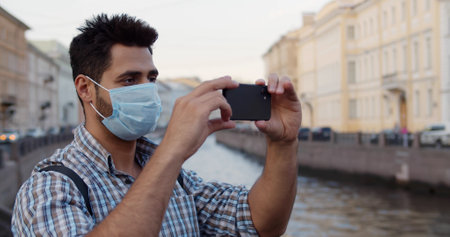 Young man traveler wearing face mask using phone on street