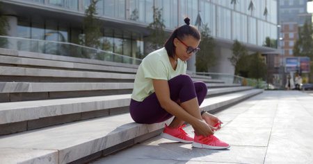 woman in sportswear tying shoe laces sitting on stairs outdoorsの写真素材