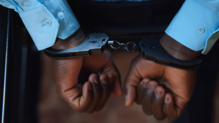 Close up of African-American criminal in handcuffs shaking hands trying to freeの写真素材