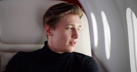 Young smiling businessman removing eyeglasses and looking out of window flying first classの写真素材