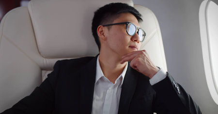 Thoughtful asian businessman on airplane looking outside windowの写真素材