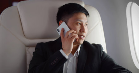 Asian businessman talking by phone on board of modern private airplaneの写真素材