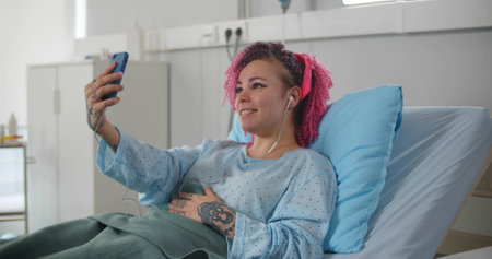 Portrait of sick woman speaking by video call in hospital and waving to camera lying in bed