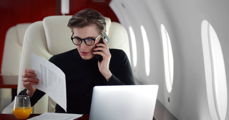 Young businessman in eyeglasses having phone call flying business class