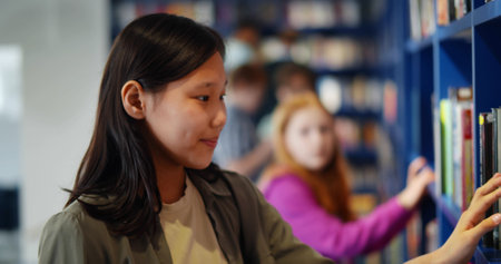 Side view of asian schoolgirl searching book on library shelfの写真素材