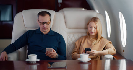 Mature couple drinking coffee and using smartphone flying on private jetの写真素材